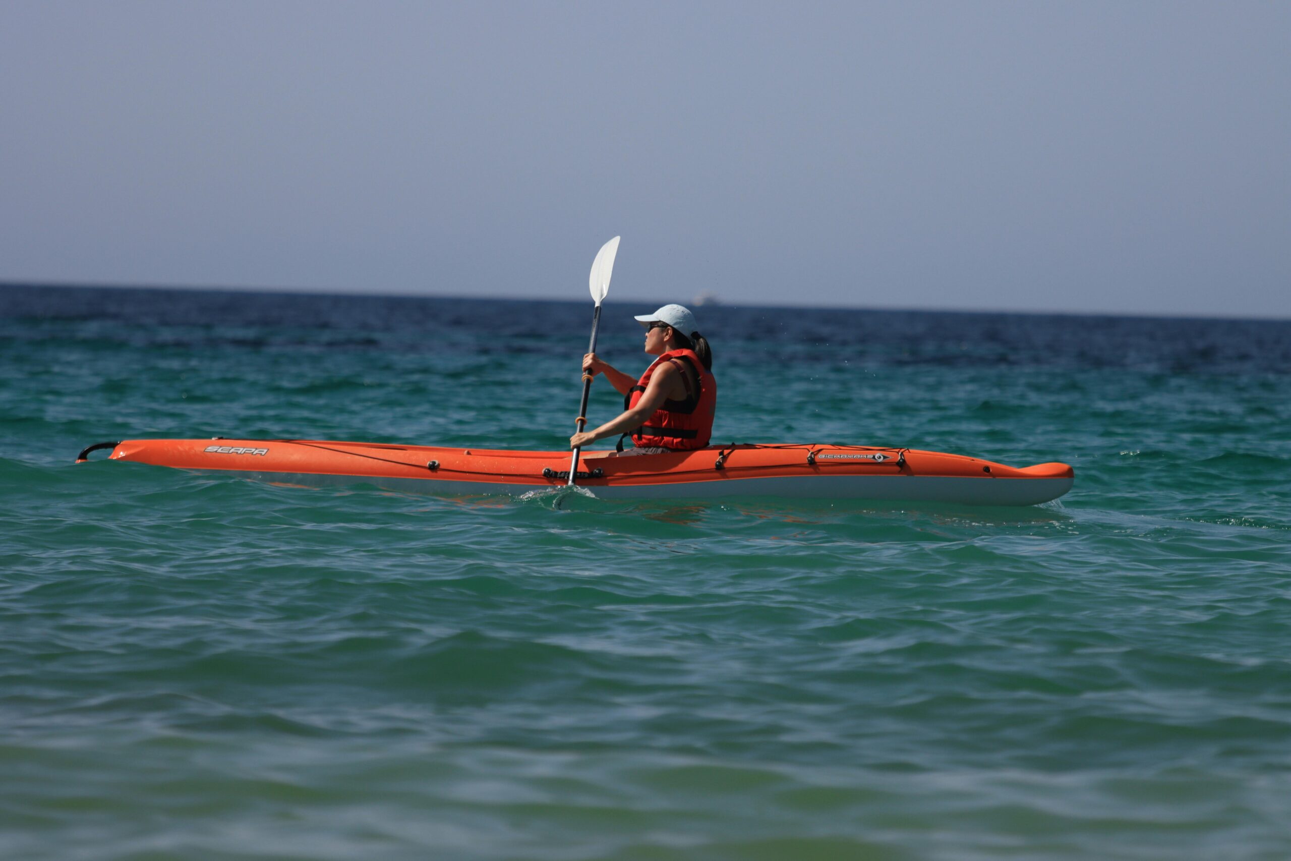 Woman kayaking in vibrant orange kayak on open ocean on a sunny summer day.